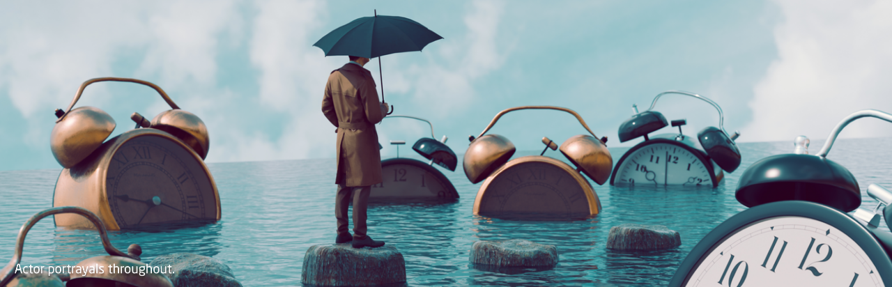 Man standing on a stone surrounded by water holding an umbrella and watching alarm clocks sink