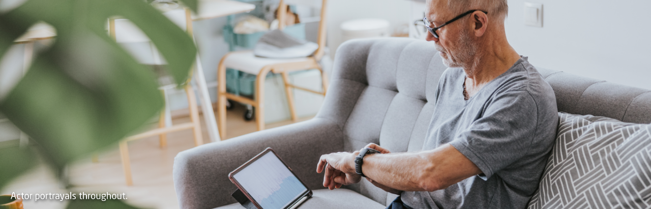 Man on sofa checking his wearable device and using a tablet
